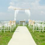 Outdoor wedding ceremony with empty white chairs and an altar adorned with a birdcage and white table.